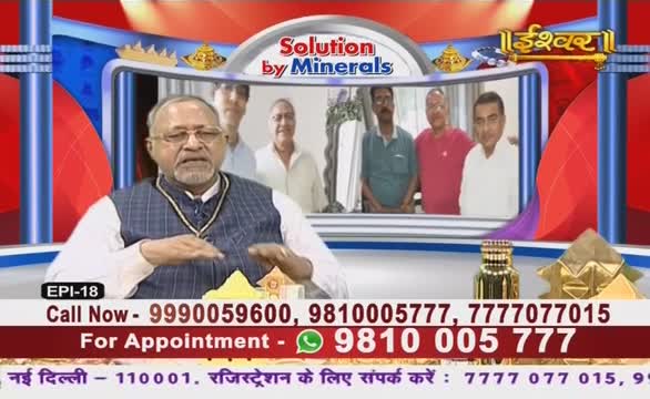 A man in a patterned vest gestures with his hands while speaking on what looks like an Ishwar Bhakti TV program in India. Behind him, a screen displays a group of men, and contact information scrolls at the bottom.
