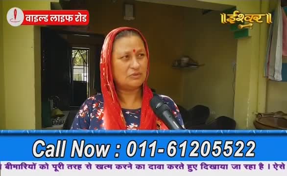 A woman in a red headscarf speaks into a microphone, likely for Ishwar Bhakti TV. A phone number flashes across the screen, promising to cure illnesses.
