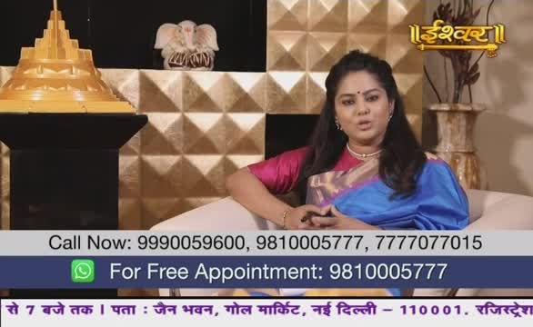 A woman, seated on a white sofa, speaks directly to the camera, her hands gesturing gently. The backdrop features a golden, geometric wall and a decorative vase, all part of the set for Ishwar Bhakti TV from India.
