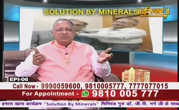 A man in a pink shirt gestures with both hands while speaking on what appears to be an Ishwar Bhakti TV program in India. Behind him, a screen displays a blurred image of two men, and contact information scrolls across the bottom.
