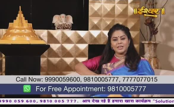 A woman in a blue and pink sari speaks directly to the camera on Ishwar Bhakti TV, with a golden structure and a small elephant statue on display behind her. The screen displays phone numbers and a WhatsApp option for free appointments, all in Hindi and English.
