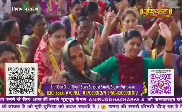 Women in colorful saris raise their arms, some with hands open, others with thumbs up, as they appear to sing or chant. The scene is broadcast on Ishwar Bhakti TV from India, with a QR code and bank details visible on the screen.
