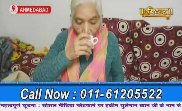 A woman in a teal sweater and pink scarf sips from a white mug, appearing on Ishwar Bhakti TV from Ahmedabad. The screen displays a phone number below her, with a call to action in Hindi.
