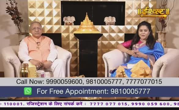 A man and a woman sit in armchairs, facing the camera on what looks like a set for Ishwar Bhakti TV in India. A golden, tiered structure sits between them, and the woman wears a blue sari.
