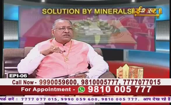 A man in a pink shirt gestures with his right hand while speaking on Ishwar Bhakti TV. The screen behind him advertises "SOLUTION BY MINERALS" in Hindi.
