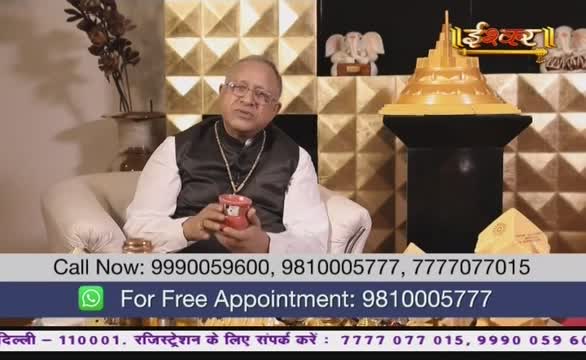 A man in a black vest and glasses sits in a beige armchair, holding a red mug, likely on Ishwar Bhakti TV in India. Behind him, a golden tiered structure and the channel's logo are visible against a geometric backdrop.
