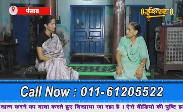 A woman in a patterned shawl sits facing another woman in a light green outfit, both on low beds. The scene, broadcast on Ishwar Bhakti TV from Punjab, is framed by a call-in number at the bottom of the screen.
