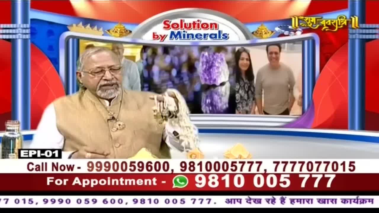 A man in a beige vest holds up a cluster of crystals on the Ishwar Bhakti TV set. Behind him, a screen displays a "Solution by Minerals" graphic and a couple in a smaller frame.
