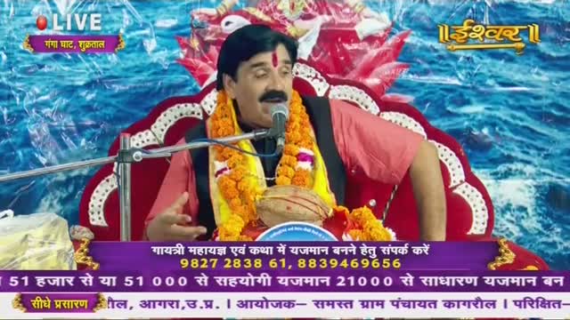 A man wearing a garland speaks into a microphone, his hand gesturing as he sits on a decorated chair. The scene is broadcast live on Ishwar Bhakti TV from India.
A man wearing a garland speaks into a microphone, his hand gesturing as he sits on a decorated chair. The scene is broadcast live on Ishwar Bhakti TV from India.