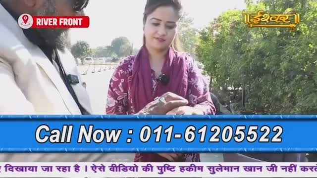 A woman in a patterned top and purple scarf is speaking, a microphone clipped to her chest. The Ishwar Bhakti TV logo and a "River Front" location marker are visible, along with a phone number for viewers in India to call.
A woman in a patterned top and purple scarf is speaking, a microphone clipped to her chest. The Ishwar Bhakti TV logo and a "River Front" location marker are visible, along with a phone number for viewers in India to call.