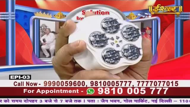 A hand holds up a white device with five circular, mesh-covered openings, likely on a TV show from India. The Ishwar Bhakti TV screen shows a man in white, and phone numbers flash below.
