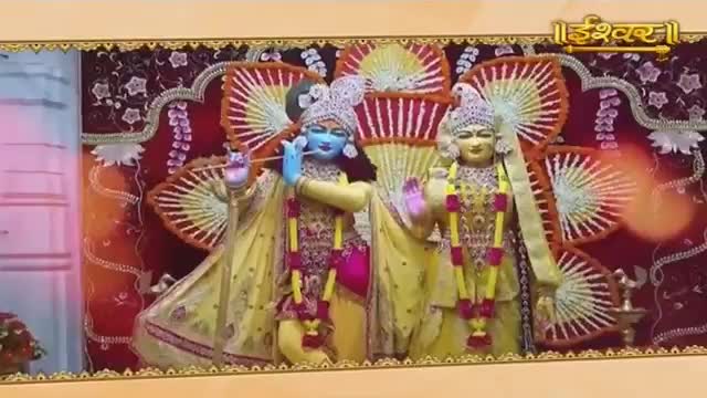 Two figures, adorned in yellow and pink, stand before a backdrop of ornate fans. One figure plays a flute, its blue face turned slightly as if in song.