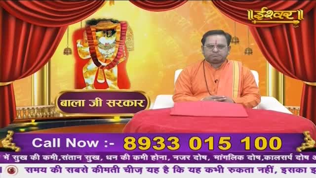 A man in an orange robe sits behind a bright red table, his hands resting in his lap. Behind him, a framed image of a deity hangs, flanked by heavy red curtains. The words "Ishwar" and "Bala Ji Sarkar" are displayed prominently.