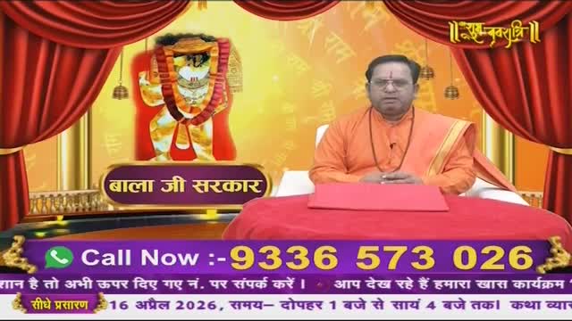 A man in an orange robe sits before a red cloth, his hands resting on a table. Behind him, a vibrant image of a deity is displayed, framed by red curtains. A phone number flashes across the bottom of the screen, advertising a program on Ishwar Bhakti TV.