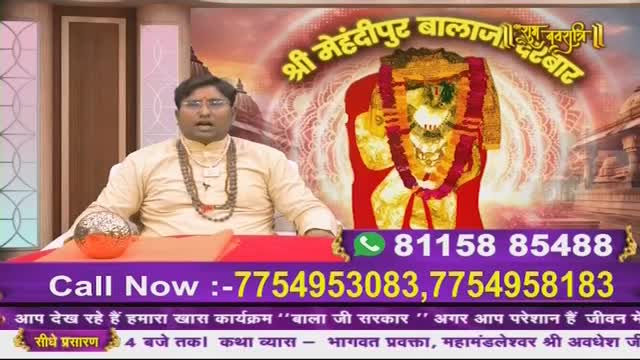 A man in a cream-colored kurta and beaded necklaces speaks intently, his mouth open. Behind him, a vibrant image of a deity adorned with garlands dominates the screen, with temple architecture in the background. Phone numbers flash across the bottom of the screen, inviting calls for a program on Ishwar Bhakti TV.