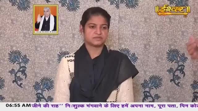 A young woman sits before a patterned backdrop, her expression serious. A framed portrait of a spiritual leader hangs on the wall behind her, and a golden inscription of "Ishwar" gleams above.