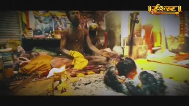 A man in a yellow cloth sits cross-legged, surrounded by offerings. The Ishwar Bhakti TV logo is visible in the corner.