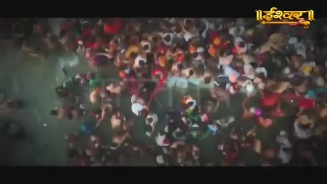 A dense crowd of people, many in vibrant saris and kurtas, are wading into the murky water. The Ishwar Bhakti TV logo is visible in the upper right corner.