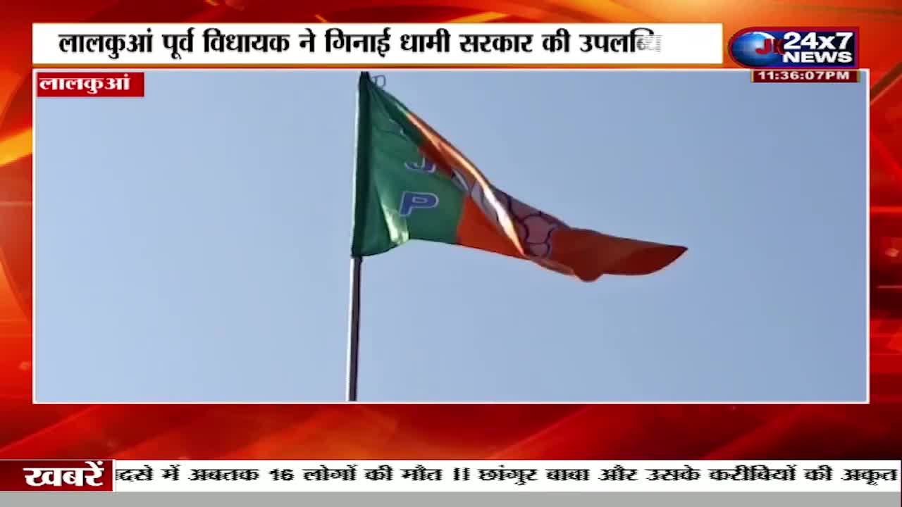 A flag, colored green and orange, billows in the wind against a clear sky. The JK 24x7 News logo is in the top right corner, with a headline about a former MLA in Lal Kuan.
