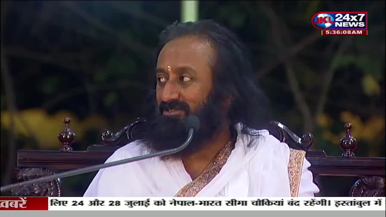 A man with a long beard and dark hair speaks into a microphone, likely on a JK 24x7 News broadcast from India. He's wearing white robes and sitting in front of a dark background.
