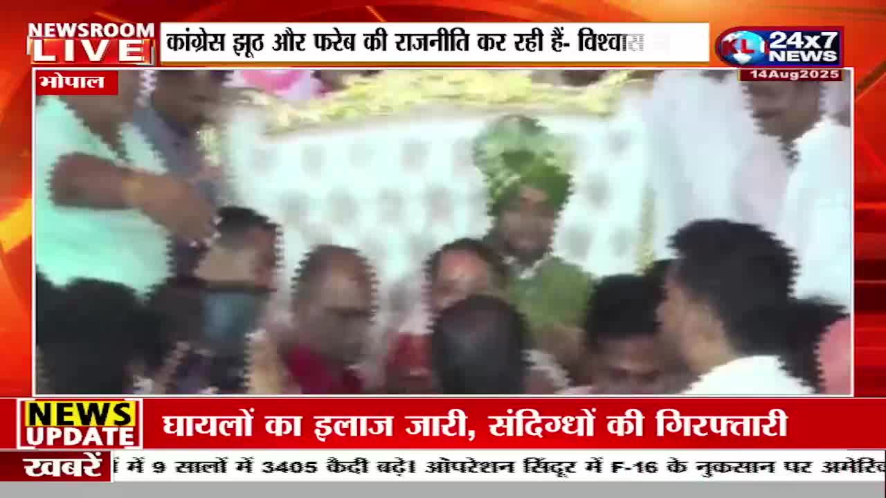 A man in a bright green turban is surrounded by others, seemingly in a procession, while a JK 24x7 News graphic displays on the screen. The news ticker at the bottom reports on medical treatment and arrests in India.
