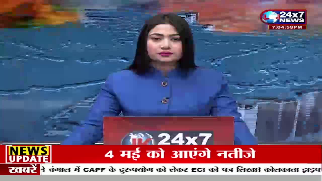 A woman in a blue jacket sits behind a news desk, her gaze fixed forward. A ticker at the bottom of the screen scrolls with Hindi text, reporting on news from India.