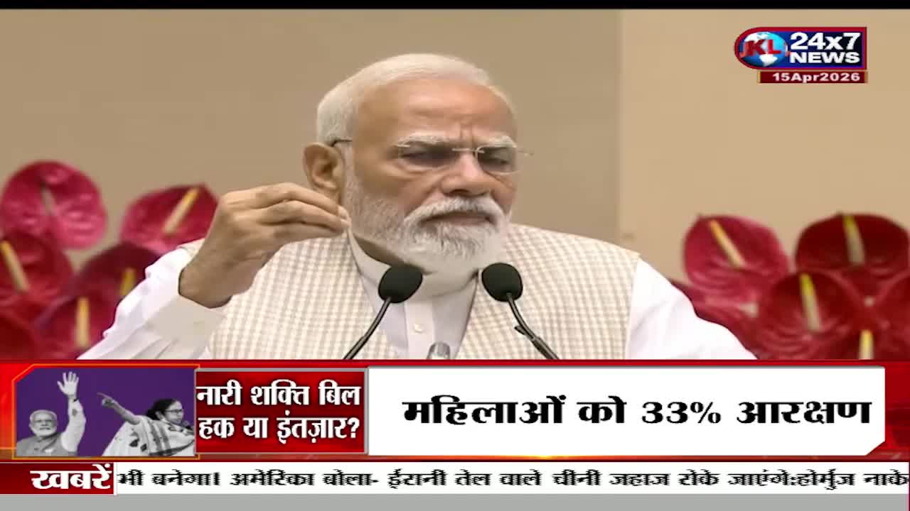 The man at the podium gestures with his right hand as he speaks. A news ticker scrolls across the bottom of the screen, displaying headlines in Hindi.