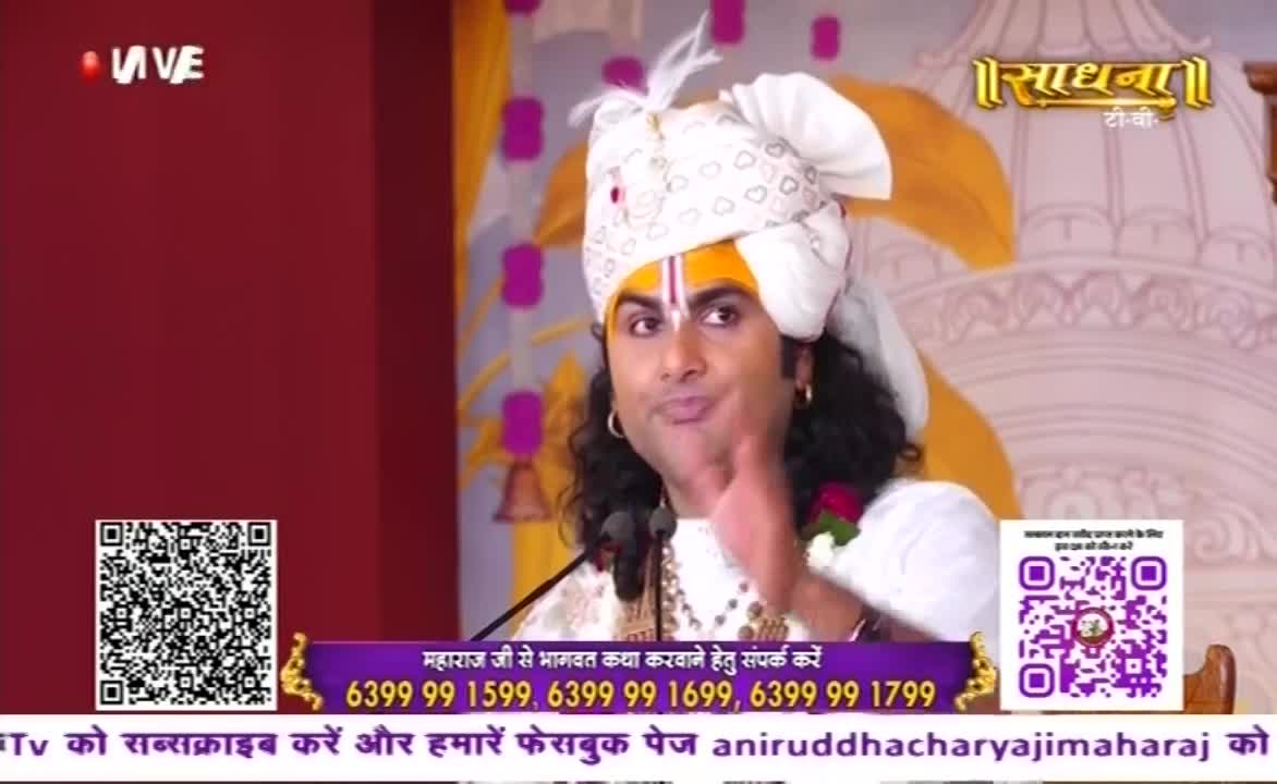A man in a turban gestures with his right hand, speaking into a microphone. The Sadhna TV logo is visible, and contact information scrolls across the bottom of the screen.
