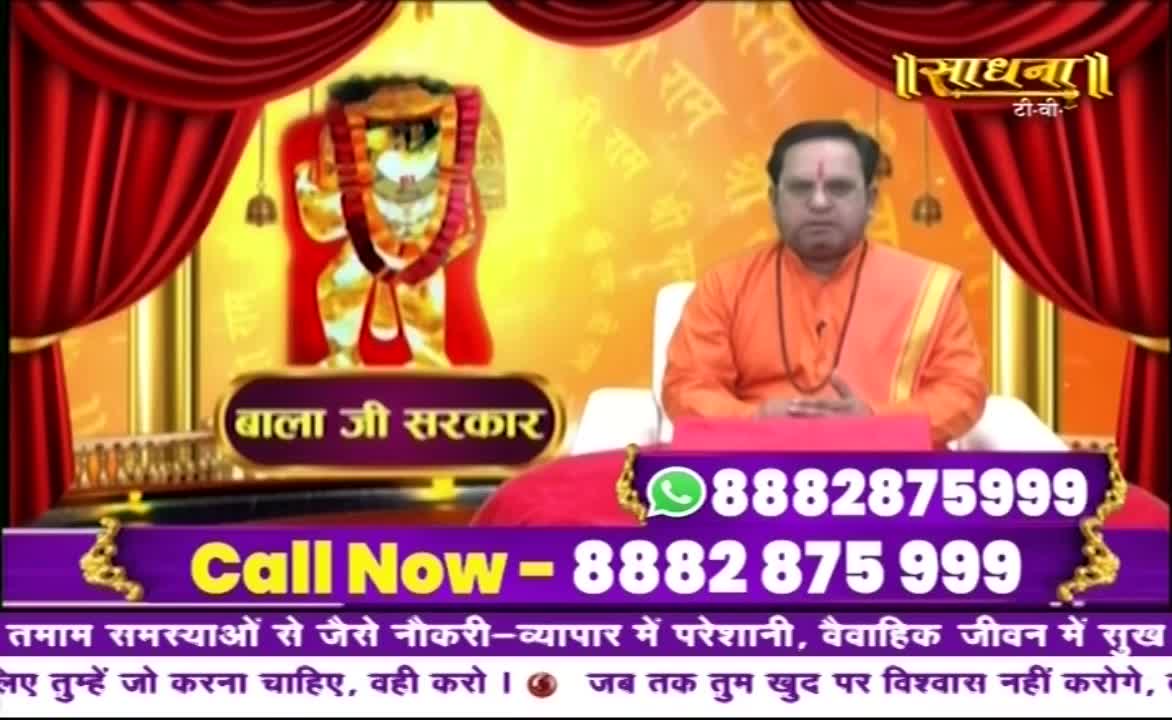 A man in orange robes sits before a backdrop of a deity, with a phone number displayed prominently below. The Sadhna TV logo is visible, and the screen invites viewers to call for help with various life problems.
