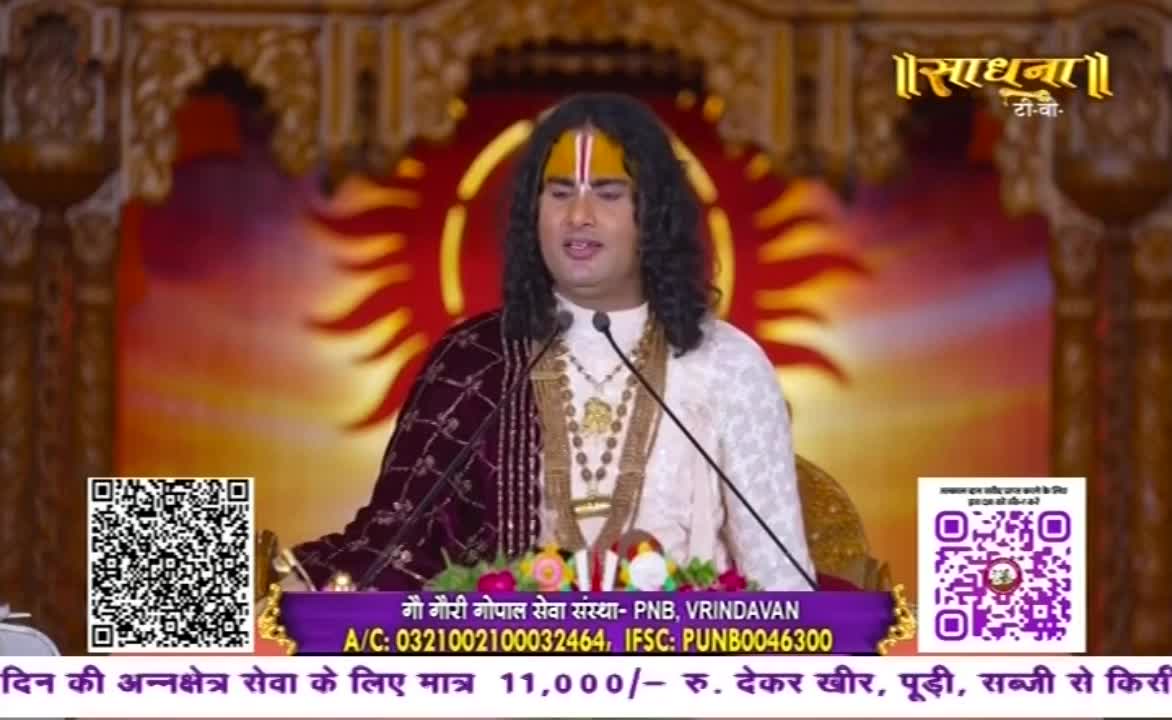 A man with a painted forehead speaks into a microphone, his words broadcast by Sadhna TV. Behind him, a vibrant backdrop glows with a sun-like design.
