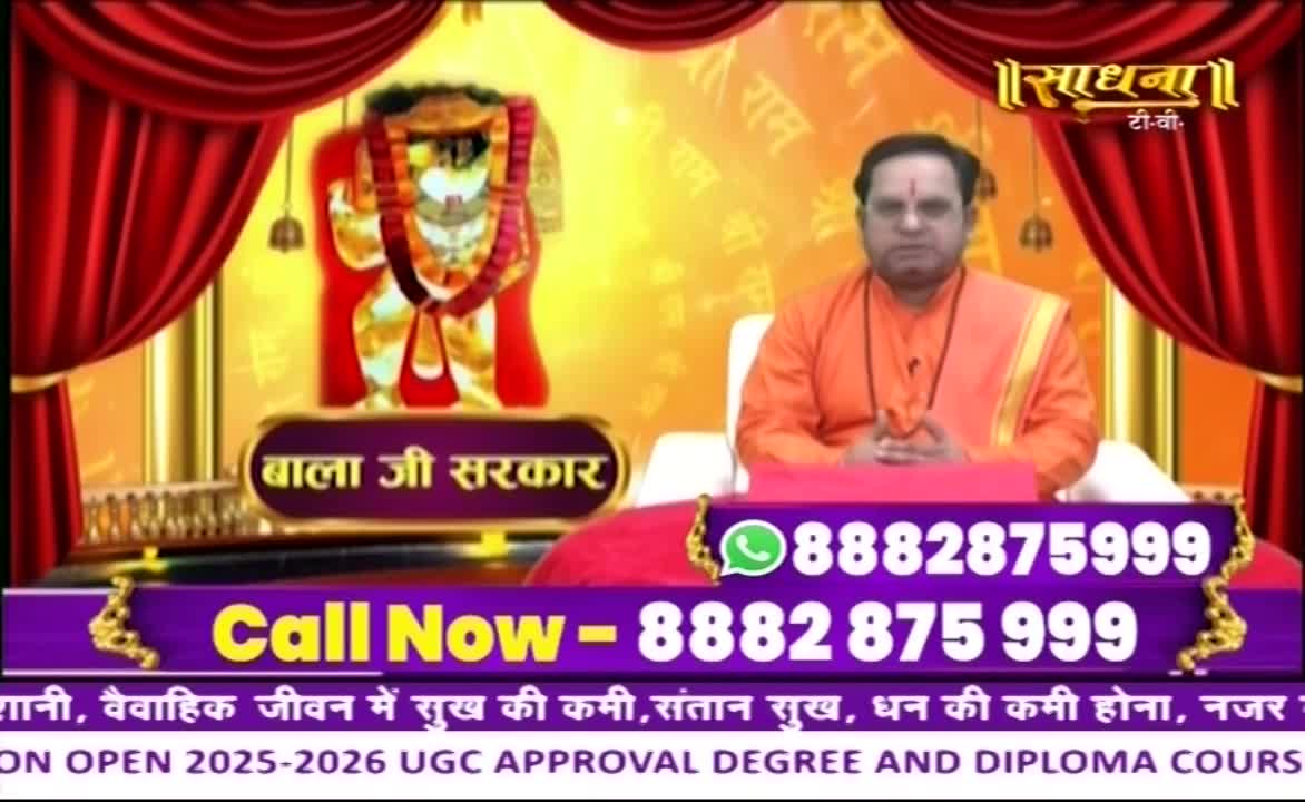 A man in saffron robes sits before a backdrop on Sadhna TV, a deity's image to his left. A phone number flashes on the screen, encouraging viewers to call.
