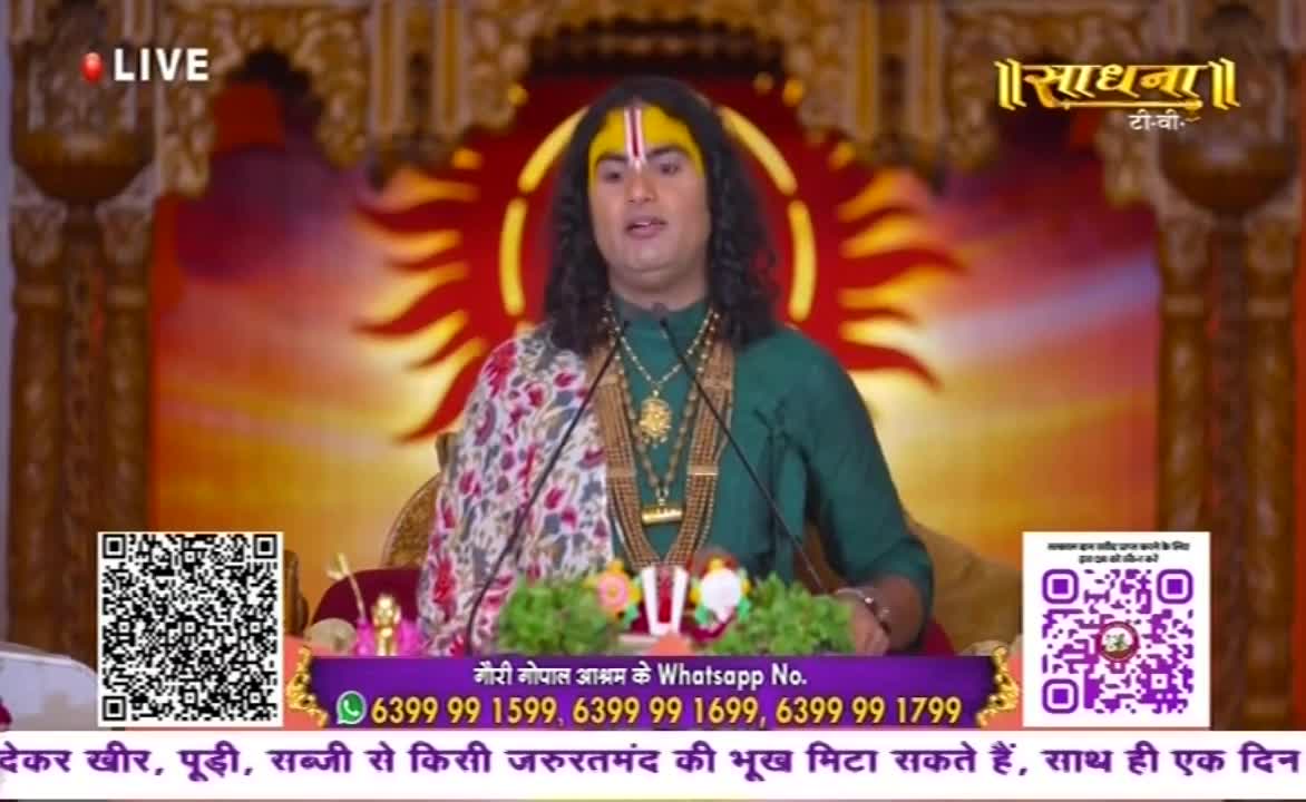 A man in a green shirt and traditional markings speaks into microphones, with a backdrop of a stylized sun. The Sadhna TV logo is visible, along with QR codes and contact information.
