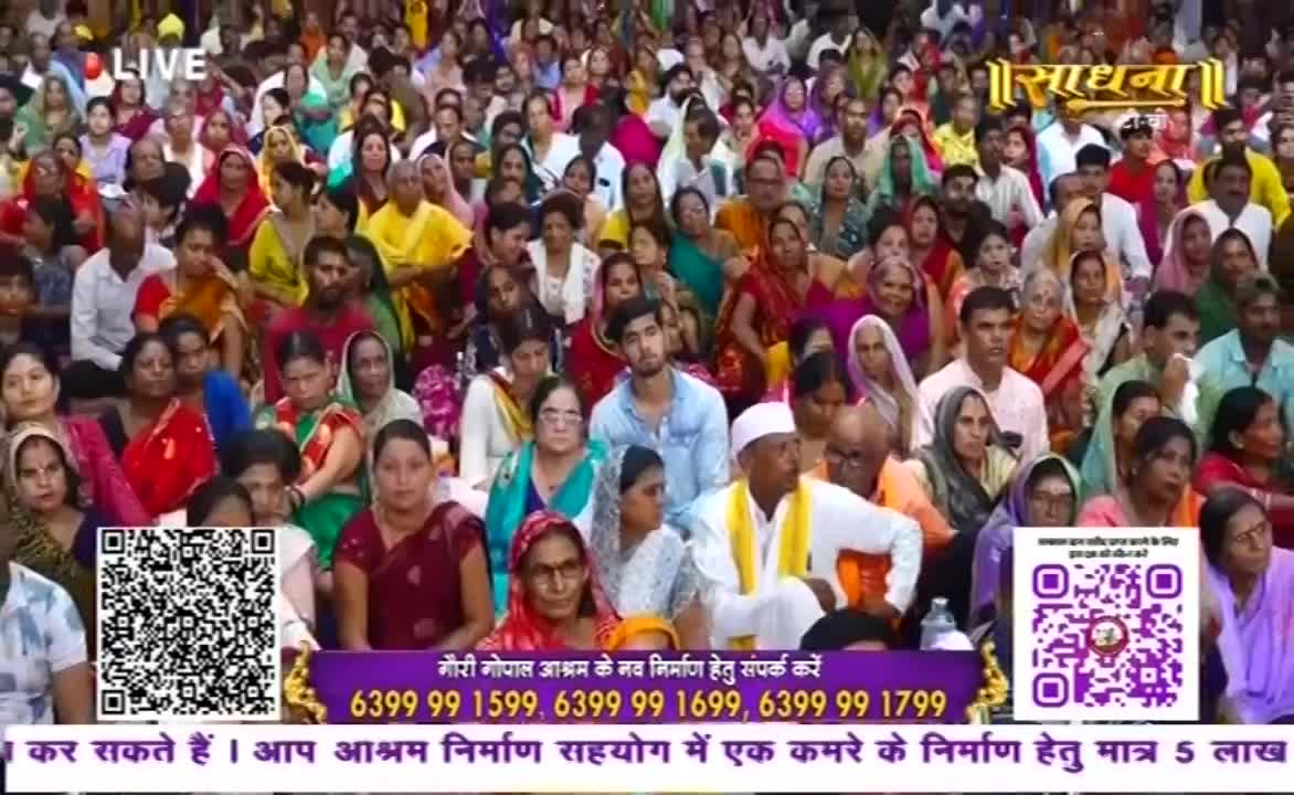 A large crowd sits closely together, many wearing colorful clothing. The word "Sadhna" is visible in the upper right corner, and a "LIVE" banner is in the top left.
