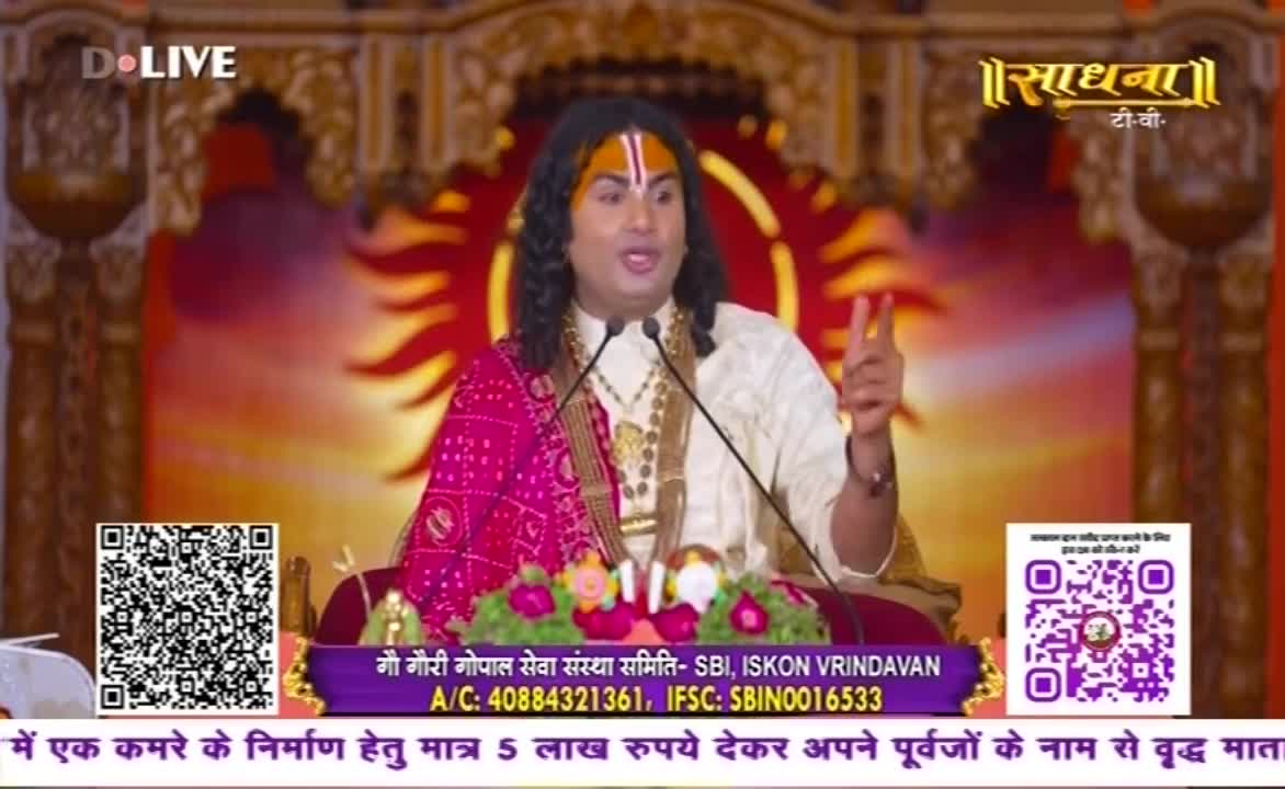 A man in a white tunic and a pink shawl gestures with two fingers, speaking into a microphone. The backdrop is a warm, stylized sun shape, and the Sadhna TV logo is visible.
