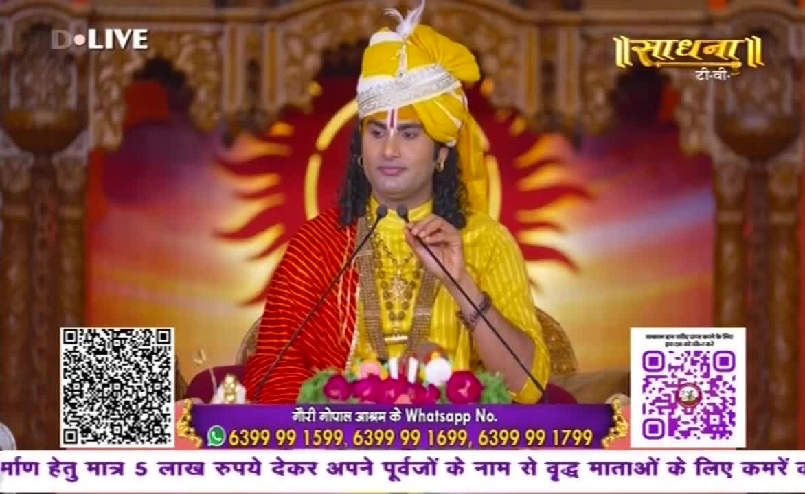 A man in a yellow turban and robes speaks into a microphone, a red shawl draped over his shoulder. The Sadhna TV logo is visible, with a QR code and phone numbers displayed below.
