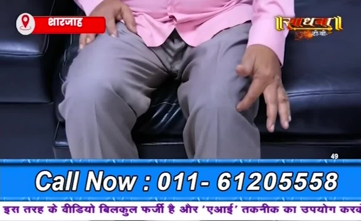 A person in a pink shirt and gray pants sits on a black leather couch. The bottom of the screen displays a phone number and a disclaimer about the video's authenticity.
