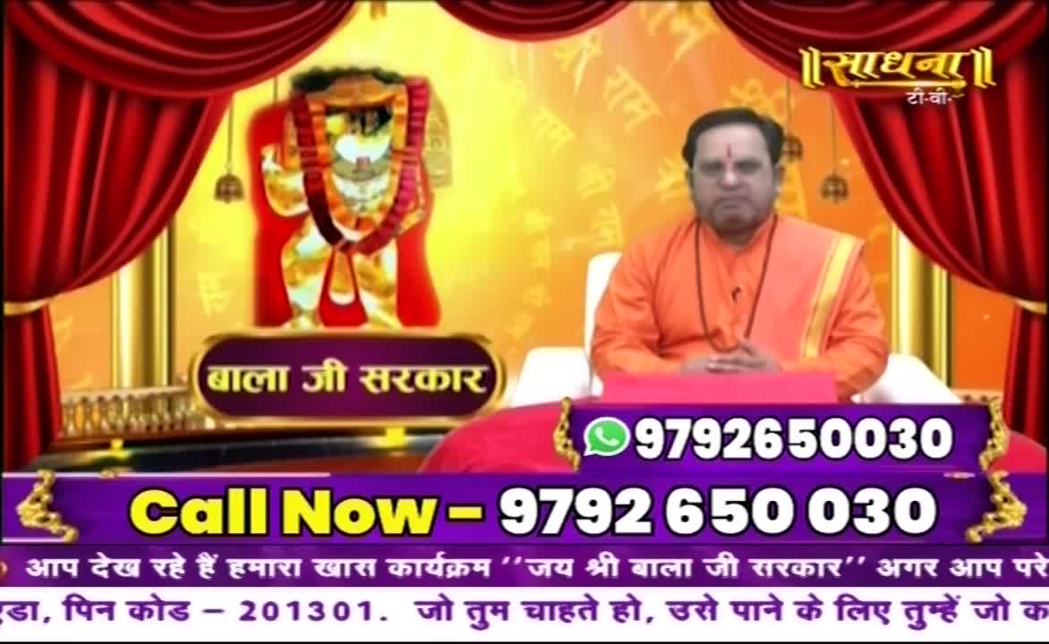 A man in saffron robes sits centered, hands clasped, against a backdrop of ornate gold and red. Below him, a phone number is prominently displayed, inviting viewers to call.
