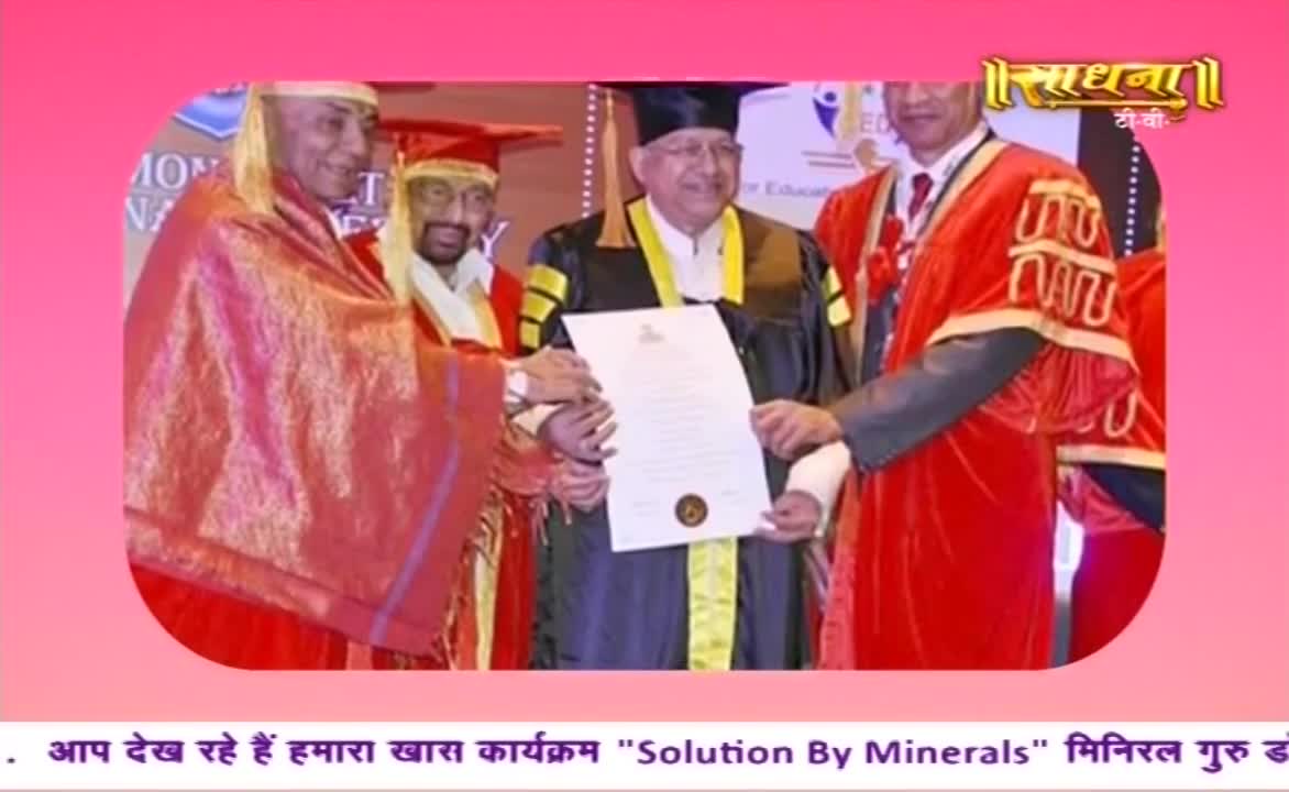A man in a black gown receives a document, held out by two others in red robes. The logo for Sadhna TV is visible in the upper right corner.
