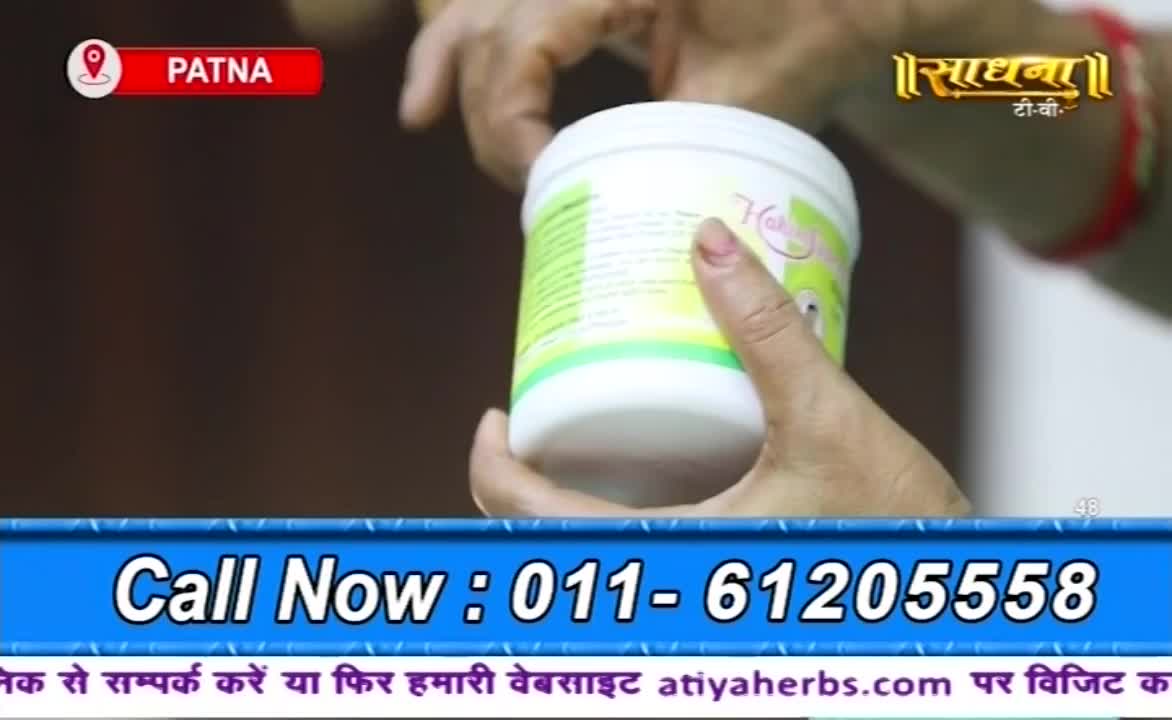 A person's hands are holding a white container, likely a product being advertised on Sadhna TV. A phone number and website address are displayed at the bottom of the screen, with a Patna location marker in the corner.
