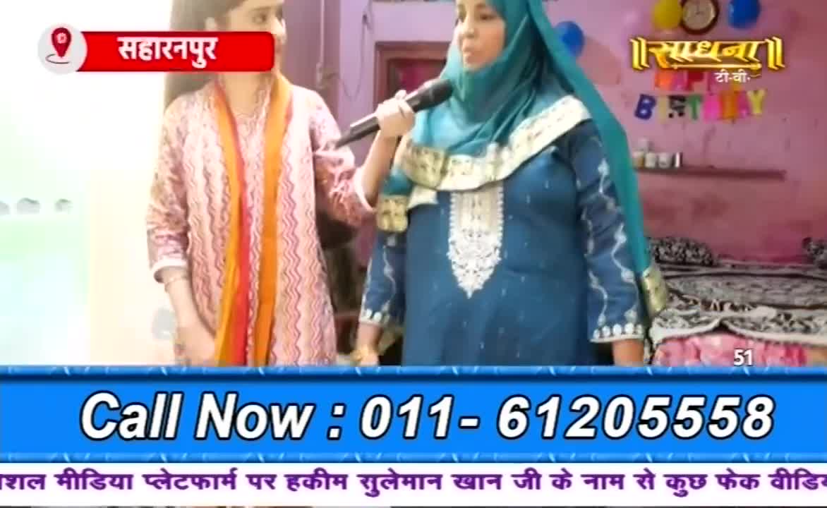 A woman in a teal hijab holds a microphone, speaking on a Sadhna TV program.  Beside her, another woman stands, wearing a patterned pink and orange outfit, with a location marker indicating Saharanpur.
