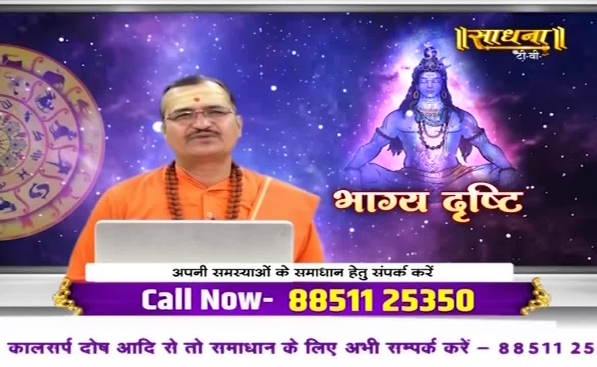 A man in orange robes, likely from India, speaks directly to the camera, a laptop in front of him. Behind him, a stylized image of a deity and the Sadhna logo fills the screen.
