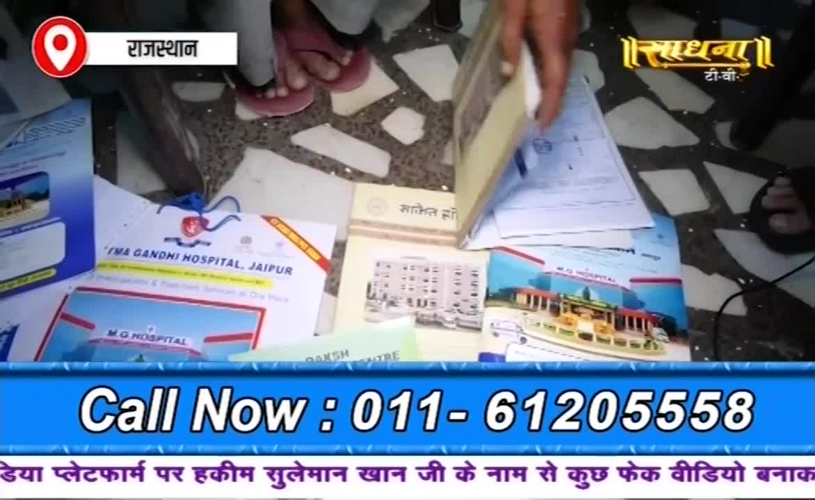 A hand is holding a book over a collection of papers and brochures, some with hospital logos. The Sadhna TV logo is visible in the top right corner, and a phone number is displayed at the bottom of the screen.
