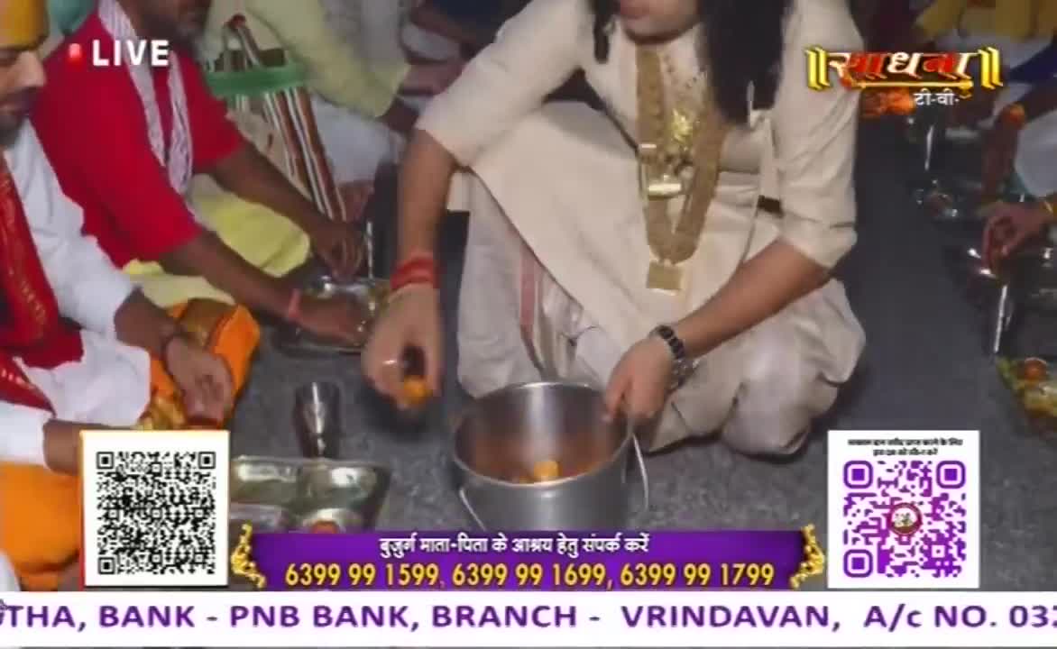 A man in a cream-colored outfit carefully places small, round, orange items into a metal pot.  Around him, others are seated, and a "LIVE" banner indicates this is a broadcast.
