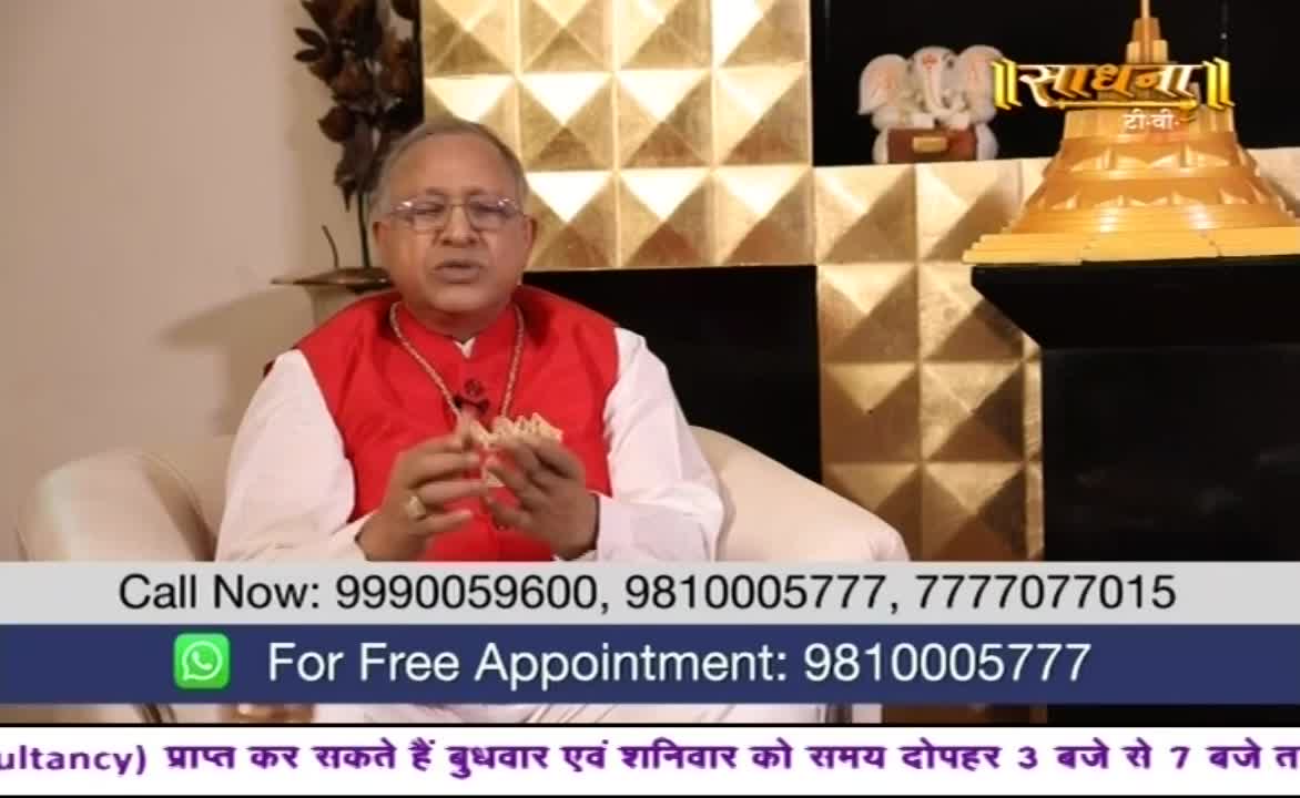 A man in a red vest and glasses gestures with his hands, speaking directly to the camera. The Sadhna TV logo is visible in the background, along with a gold-patterned wall.
