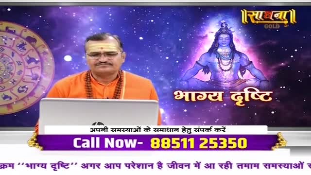 A man in saffron robes sits behind a laptop, speaking on a television program called "Sadhna Gold." Behind him, an image of a deity and the words "Bhagya Drishti" are displayed.

