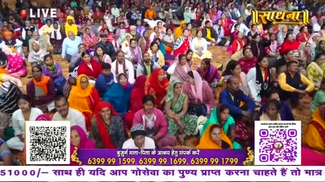 A large crowd sits close together, many in colorful headscarves and shawls, listening to something off-camera. The Sadhna logo and a "LIVE" banner are visible, suggesting a broadcast.
