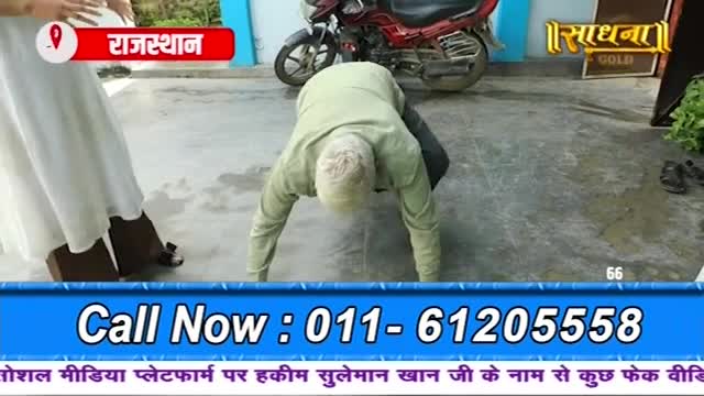 A man in a light green shirt bends low, his hands on the ground, as if preparing to crawl. A woman in a white dress stands nearby, and a motorcycle sits in the background.
