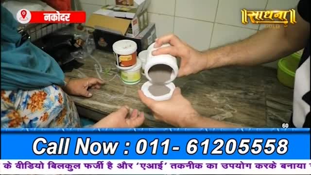 A man is pouring a gray substance from a white container onto a small, white disc. Beside him, a woman watches, her hands resting on the counter.
