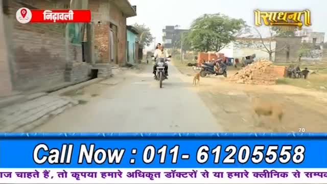 A man rides a motorcycle down a dusty road in India. A dog trots alongside him, and another dog is further ahead.