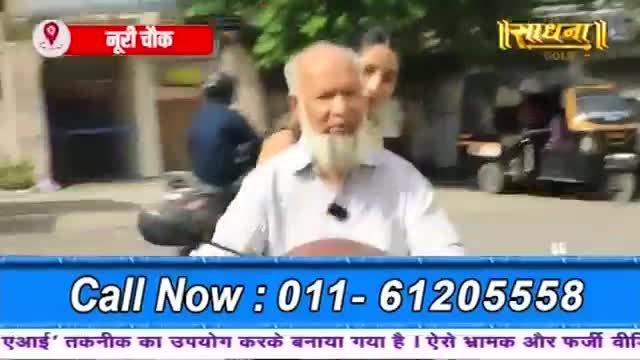 A man with a long white beard is riding a scooter, a woman behind him. An auto-rickshaw passes by on the street.